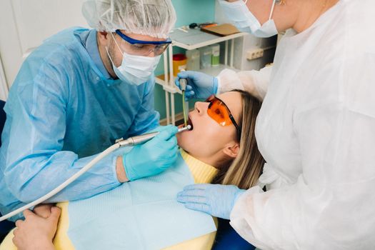 A male dentist with dental tools drills the teeth of a patient with an assistant. The concept of medicine, dentistry and healthcare.