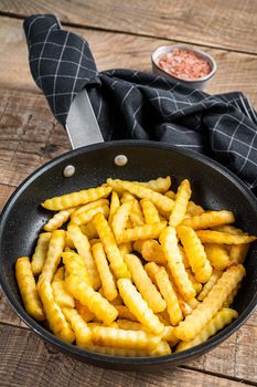Fried Crinkle oven French fries potatoes sticks in a pan. Wooden background. Top view.