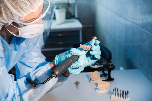 A masked and gloved dental technician works on a prosthetic tooth in his lab.