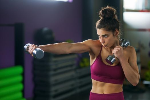 Sporty woman punching and boxing with dumbbells. Hard exercising and training at the gym. Fitness concept.