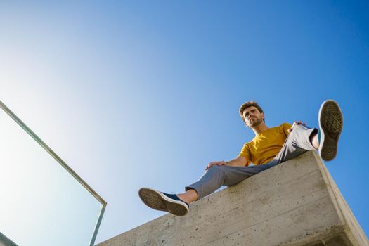 Young man sitting on a ledge looking around