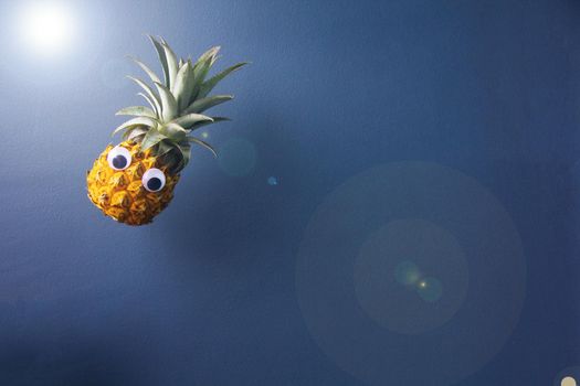Fresh pineapple with googly eyes looks like flying, hang on air on blue background, enough place for text. Good concept for magic.