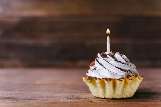 Birthday cream cupcake with candle on a wooden background. Copy-space in left part of image.