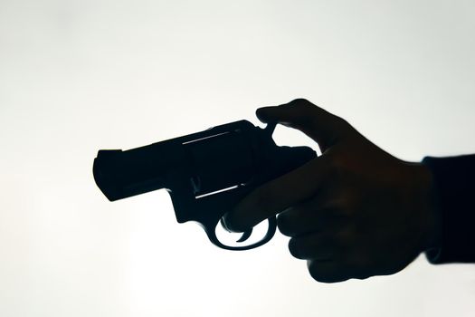 Silhouette of hand with gun on white background. Man pulls the trigger of revolver to fire. Criminal with pistol close up. Firearm for attack or defense.
