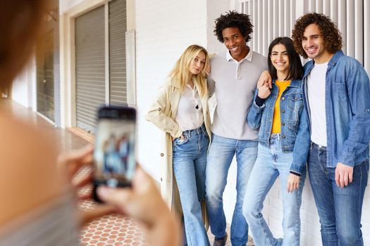 Multi-ethnic group of friends taking photos with a smartphone in the street. Young people having fun together.