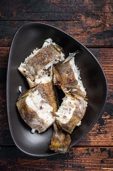 Roasted hake white fish in a plate. Dark wooden background. Top view.