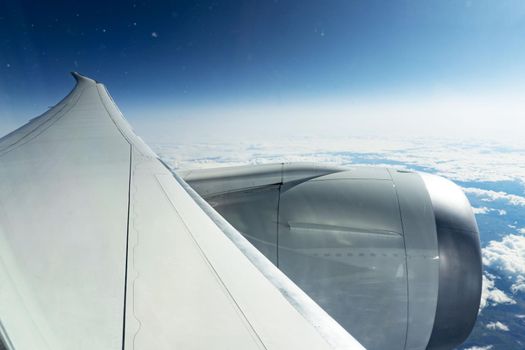 Cloudy view and the wing of plane through the aircraft window from the seat at a plane, high at the sky, somewhere at stratosphere..