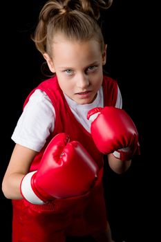 Sporty teenage girl doing boxing exercises. Close up portrait of pretty girl in red sports uniform making direct hit. Preteen child posing in studio against black background