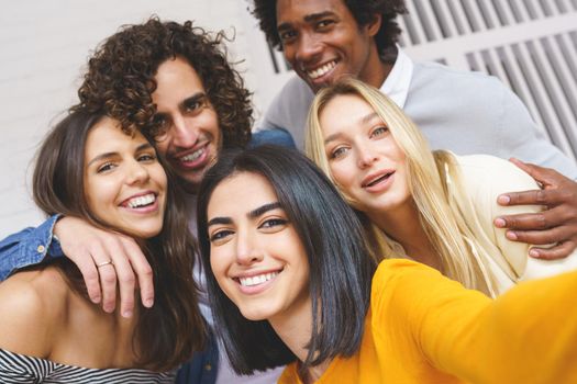 Multi-ethnic group of friends taking a selfie together while having fun in the street. Persian woman in the foreground.