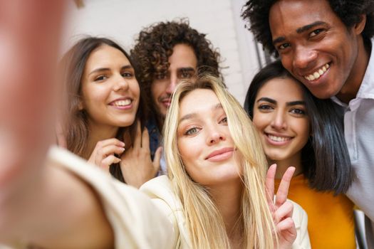 Multi-ethnic group of friends taking a selfie together while having fun in the street. Blonde Russian woman in the foreground.