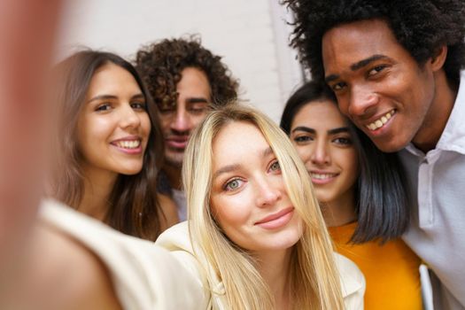 Multi-ethnic group of friends taking a selfie together while having fun in the street. Blonde Russian woman in the foreground.