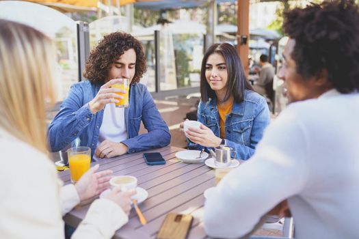 Multi-ethnic group of friends having a drink together in an outdoor bar. One of the men shows something on his smartphone to his friends.