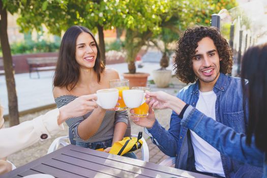 Multi-ethnic group of friends making a toast with their drinks while having a drink together at the outside table of a bar.