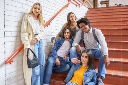 Group of friends with ethnic variety, sitting on some street steps having fun together outdoors.