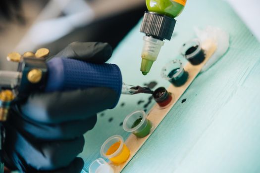 Female tattooist loading the tattoo machine with ink by mixing different colours. Tattoo concept.