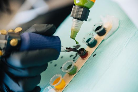 Female tattooist loading the tattoo machine with ink by mixing different colours. Tattoo concept.