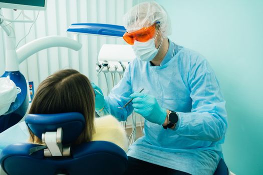 a dentist wearing a protective mask sits nearby and holds instruments in his hands before treating a patient in the dental office.