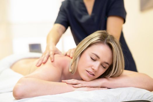 Young woman lying on a stretcher receiving a back massage in a physiotherapy center.