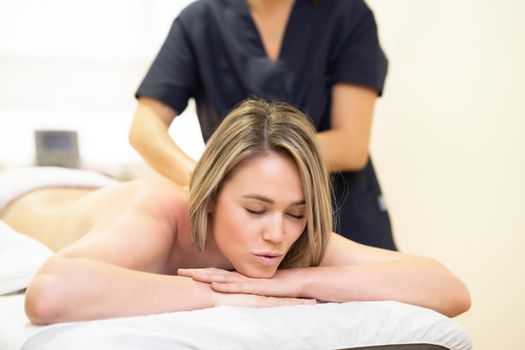 Young woman lying on a stretcher receiving a back massage in a spa center.