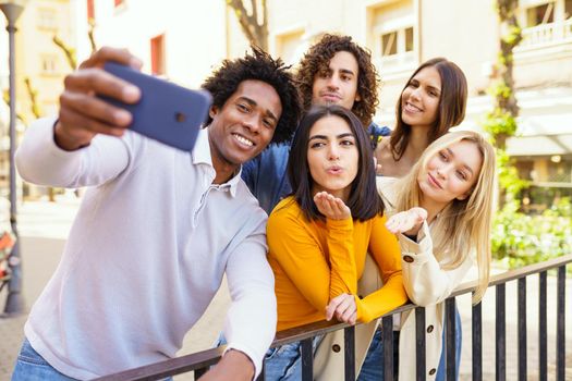 Multi-ethnic group of friends taking a selfie in the street with a smartphone. Young people having fun together.