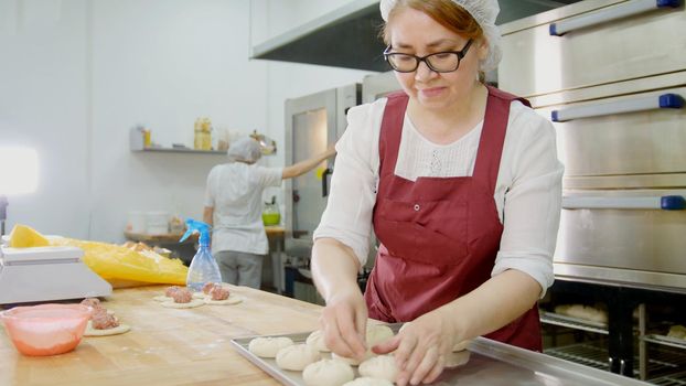 Woman in glasses and apron bakes cakes in the bakery, close-up