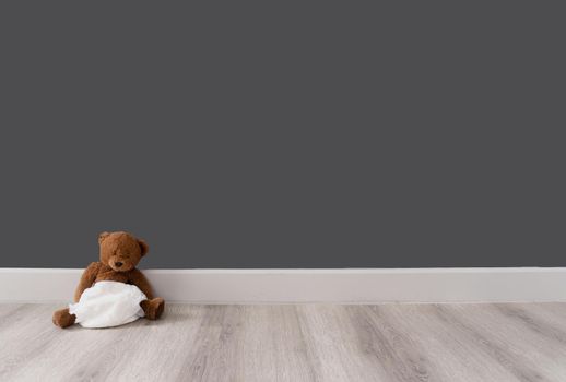 Brown bear in diaper sits near grey wall, good background, enough space for text, concept of loneliness