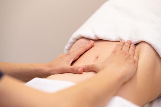 Woman receiving a belly massage at spa salon. Female patient is receiving treatment by professional osteopathy therapist.