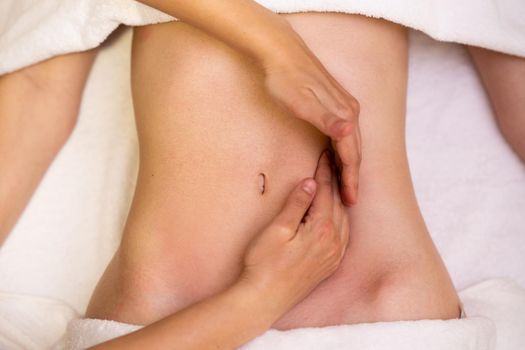 Top view of hands massaging female abdomen in a physiotherapy center. Therapist applying pressure on belly