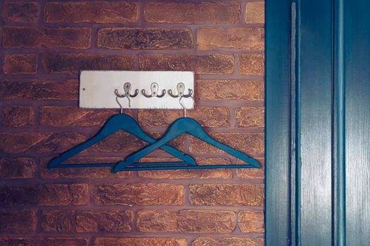 Two color hanger on hooks hanging on brick wall near door, creative loft style, toned in blue, indoors, copyspace,