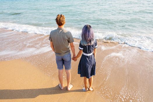 Couple in love standing on sand beach and holding hands, enjoying view of sea on travel summer vacations.