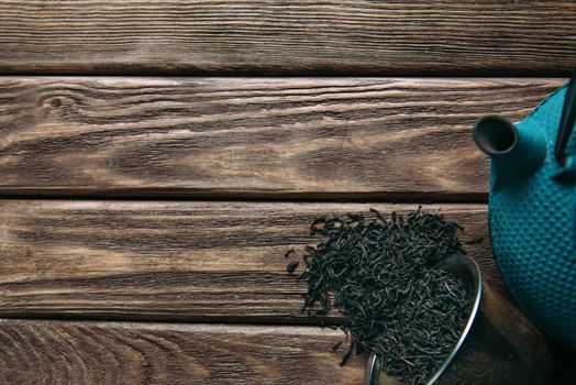 Iron teapot and dry leaves of black tea on a wooden background, top view. Space for text in left part of the image.
