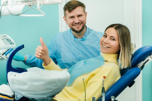 Beautiful girl patient shows the class with her hand while sitting in the Dentist's chair.