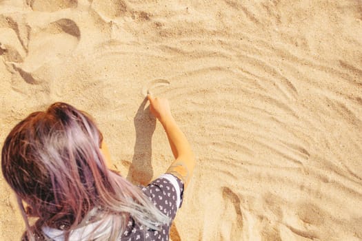Young woman draws on the sand with her finger, top view.