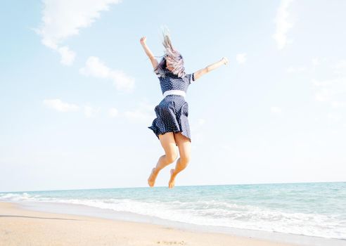 Happy young woman jumping on sand beach near the sea, summer vacations.