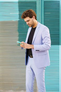Young businessman wearing a suit texting with smartphone outdoors.
