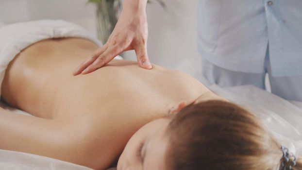 Blonde young woman model receiving relaxing massage in spa room, close up view