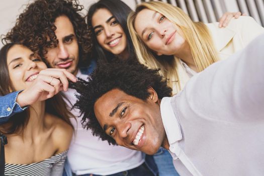 Multi-ethnic group of friends taking a selfie together while having fun in the street. Black man with afro hair in the foreground.