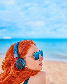 Redhead woman listening to music on the beach. Sexy woman listening to the music on the beach. The concept of vacation. Relax on the ocean.