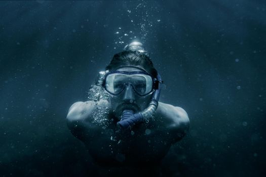 Freediver young man in mask and snorkel swimming underwater among sunbeams, front view.