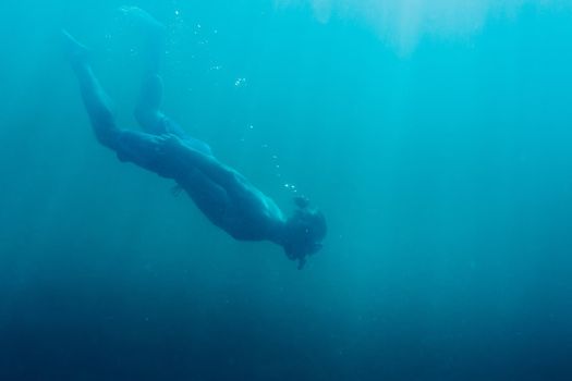 Young man free diver swimming underwater in deep sea with mask and snorkel.