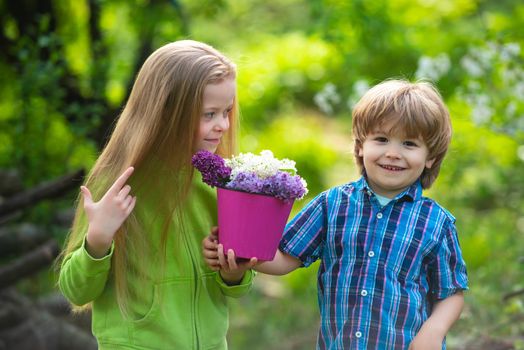 Cute children gardening and planting flowers to the ground in spring garden, seasonal outdoor activities, happy childhood