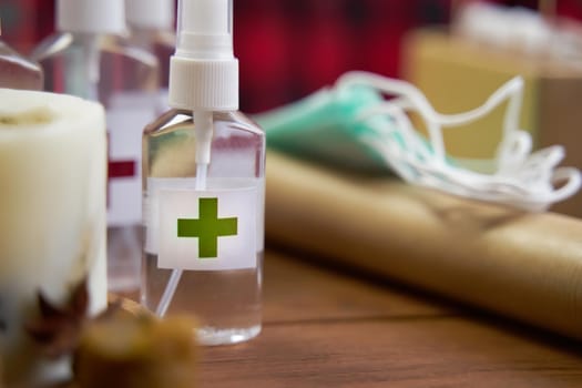 Alcohol antiseptic with the green cross logo on wooden background. Sanitizer, medical masks and roll of paper on table. Concept of hand hygiene and prevention from viruses and bacteria.