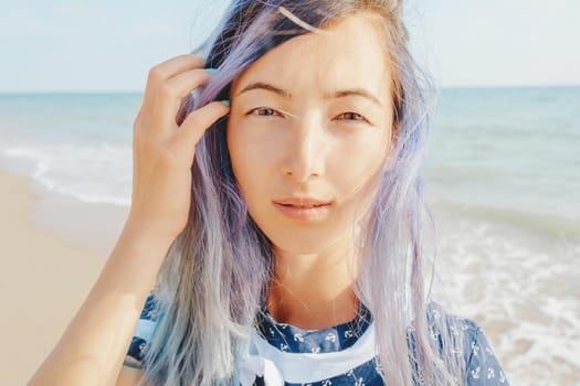 Portrait of beautiful girl with violet hair on background sea, looking at camera.