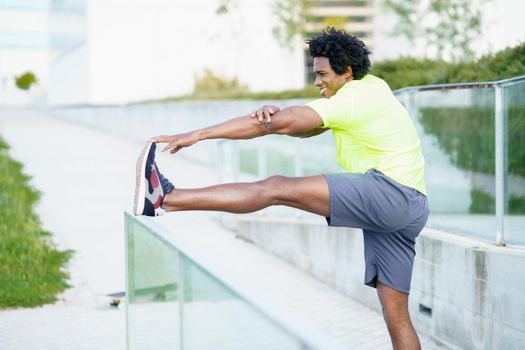 Black man with afro hair doing stretching after running outdoors. Young male exercising in urban background.