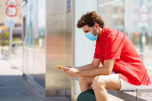 Student male wearing a surgical mask while waiting for a train at an outside station