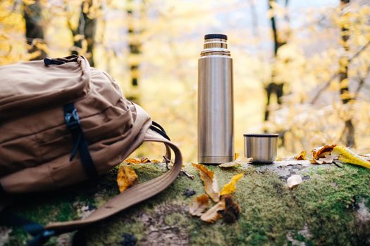 Backpack and thermos on fallen tree trunk in autumn forest.