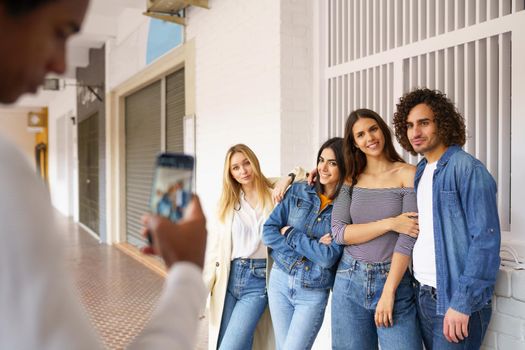 Multi-ethnic group of friends taking photos with a smartphone in the street. Young people having fun together.