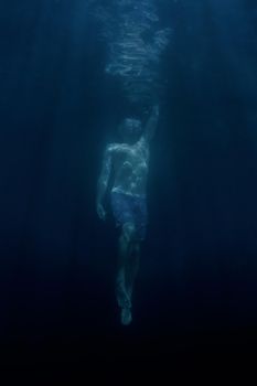 Young man freediver swimming up to the water surface.