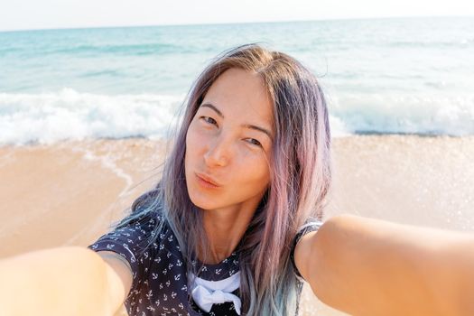 Beautiful young woman taking selfie on sand beach near the sea, point of view.