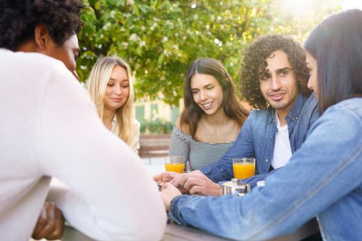 Multi-ethnic group of friends having a drink together in an outdoor bar. One of the men shows something on his smartphone to his friends.